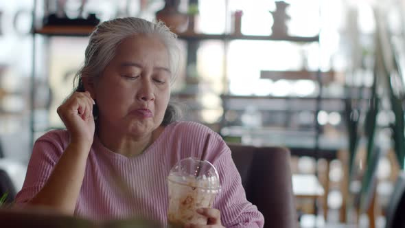 Asian senior woman drinking ice chocolate happily in coffee shop