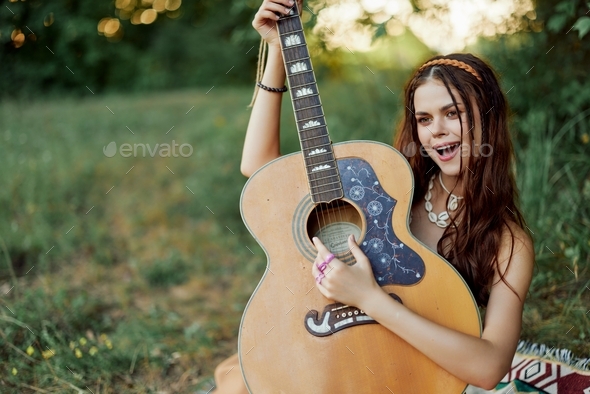 Beautiful woman playing guitar in nature in a hippie summer look, singing songs style of life