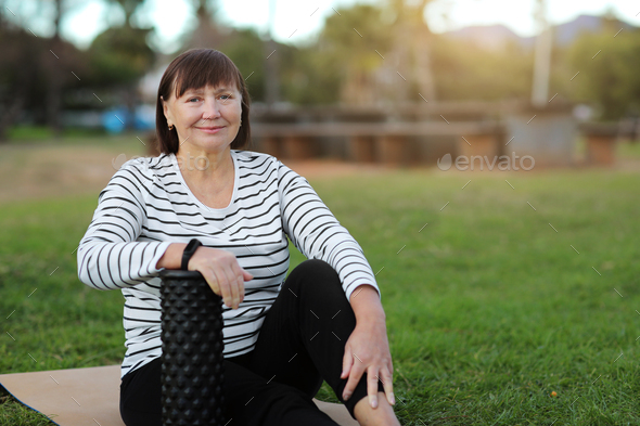 Smiling middle aged sportive woman in casual sportswear sitting on yoga mat and relaxation after wor