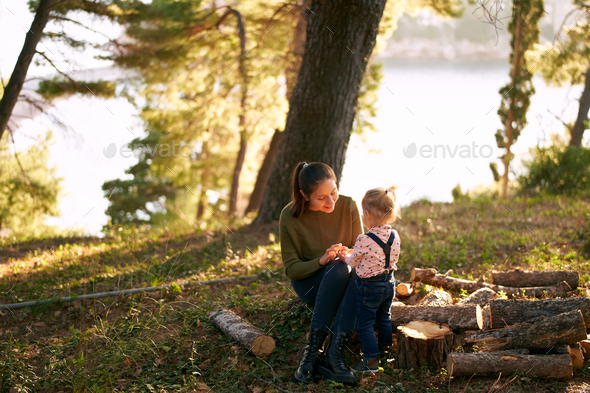 Mom teaches a little girl to count on her fingers sitting on a stump in a clearing in the forest