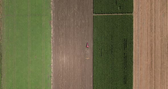 Red tractor flattening a field for seeding, Drone follow footage. alt