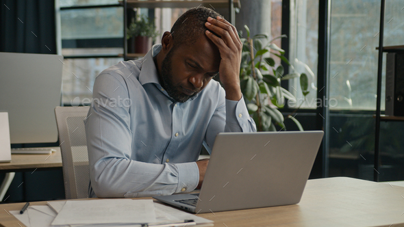 Overworked African American mature man working laptop in office suffer with eye strain exhausted