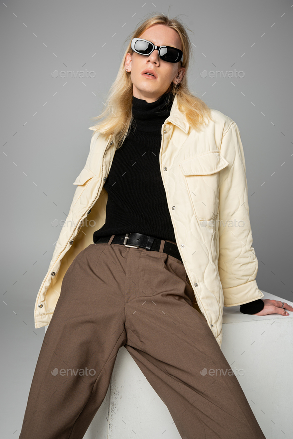 vertical shot of young handsome non binary person in stylish attire posing on cube, fashion concept