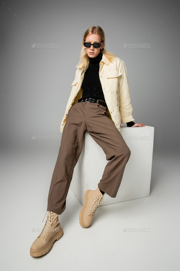 good looking non binary person in trendy attire with sunglasses posing on cube looking at camera