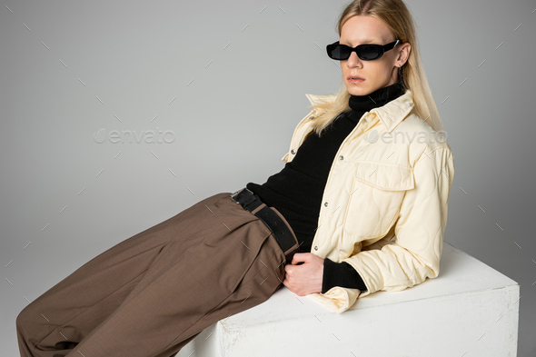 young androgynous person in elegant warm attire posing on huge white cube, fashion concept