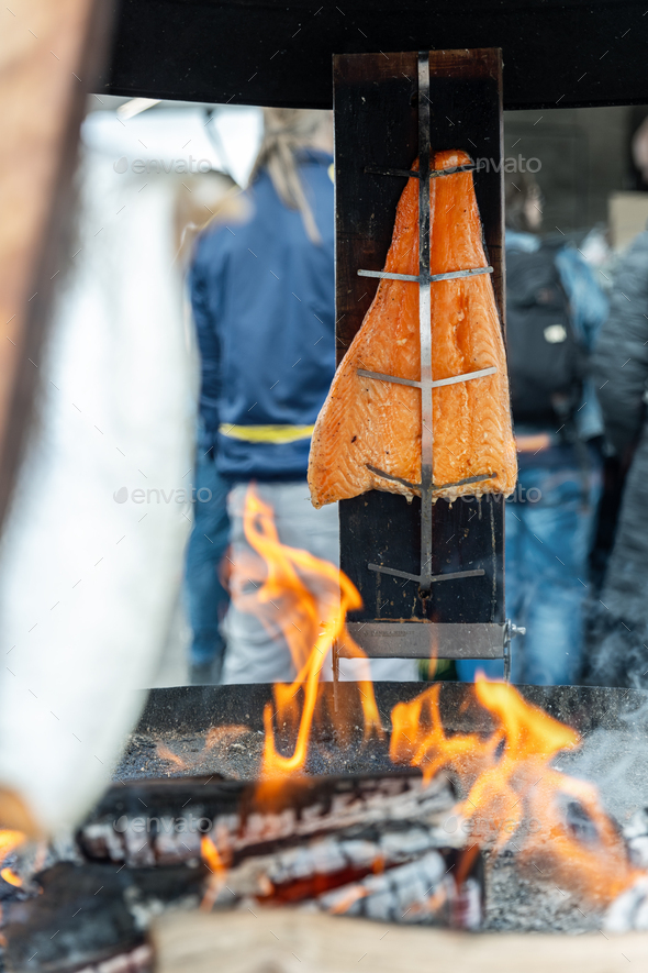 Smoked salmon fish fillet pinned on wooden plank board grilled on open fire pit outdoors