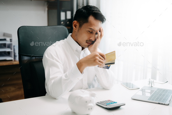 Financial owe, Asian man sitting, holding credit card, stressed