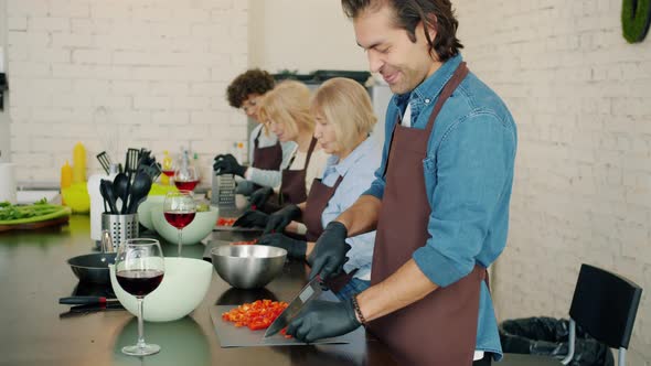 Joyful Man and Women in Aprons Chopping Vegetables in Kitchen During Cooking Class alt