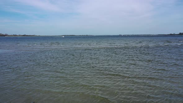 A low angle drone shot over a beach, looking out at the water & the horizon. It is at low tide on a alt