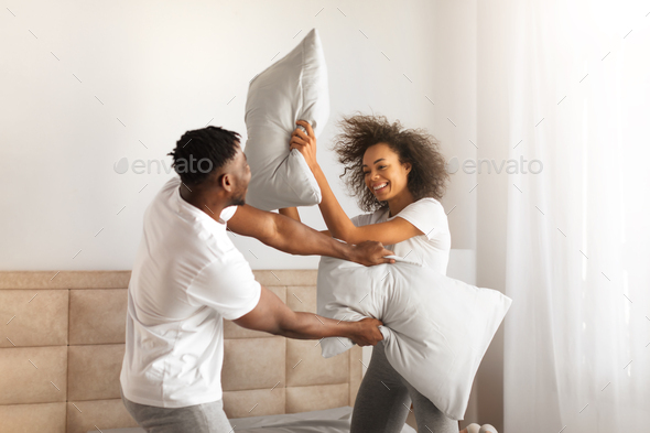 Joyful African Couple Having Pillow Fight For Fun In Bedroom