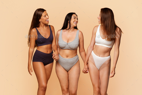 Three diverse young women in underwear holding hands and laughing together  Stock Photo by Prostock-studio
