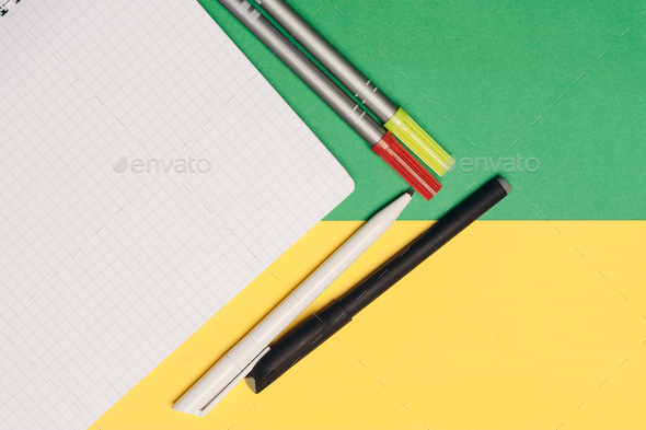 notepad pens and markers on yellow green background top view