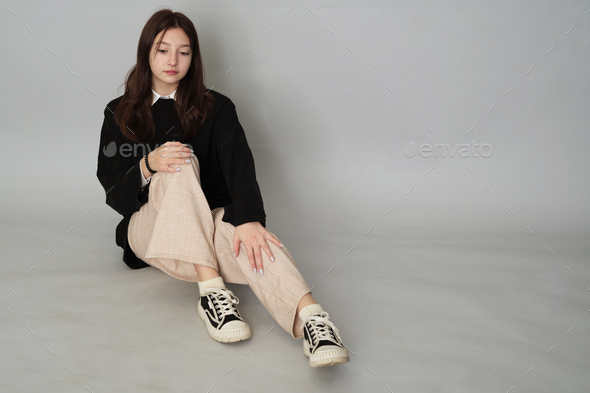 Teen girl crouched in a relaxed pose, dressed in a black hoodie, pairing it with neutral-toned