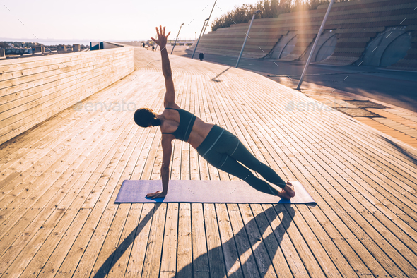 Slim woman training on yoga mat on wooden promenade Stock Photo by