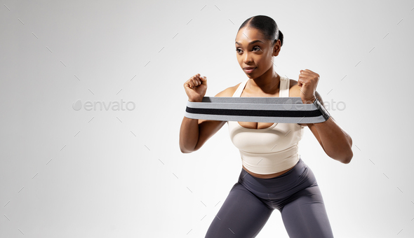 Black athletic lady exercising with rubber resistance band, white backdrop