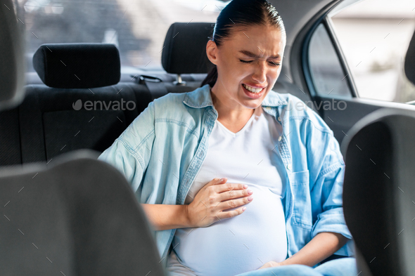 Pregnant lady in car suffering from labor pains clutching abdomen