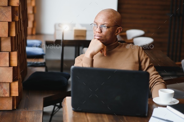 African-Ameican entrepreneur wearing shirt with rolled up sleeves looking through window