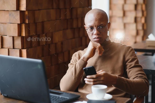 African-Ameican entrepreneur wearing shirt with rolled up sleeves looking through window