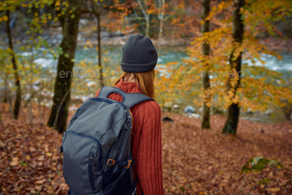 woman in a sweater with a backpack on her back near the river in