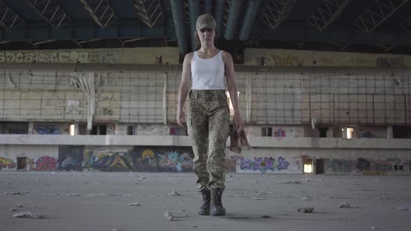 Attractive Young Woman in Military Uniform Walking Slowly in Dusty Dirty Abandoned Building Carrying alt