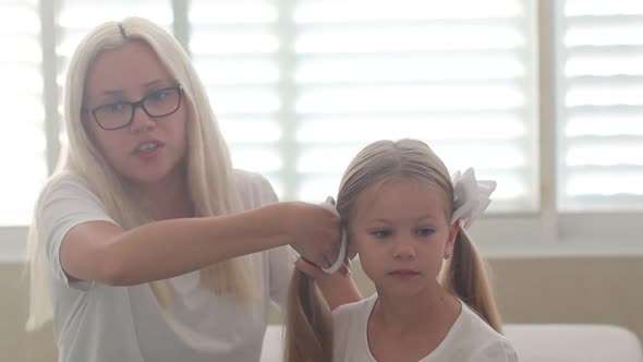 Mom Combs Hair to a Little Girl with Blue Eyes
