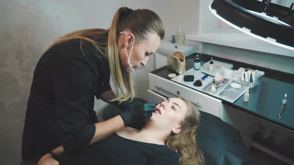 The Master in a Beauty Salon Draws a Contour with a Pencil on the Lips of a Young Woman alt