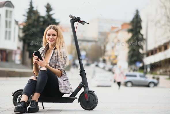 young woman on electro scooter in city. woman riding scooter in sunset light in street