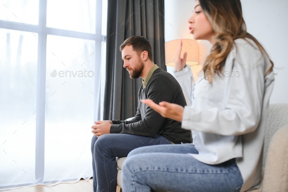 Beautiful couple is sitting back to back on the couch while having a quarrel