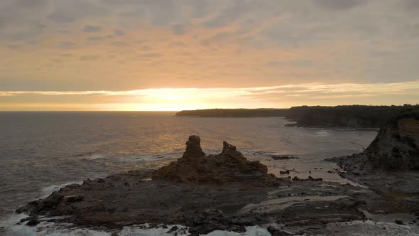 A high up forward moving aerial of eagles nest rock formation on bass coast Victoria with the sun se alt