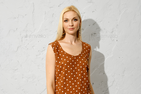 Fashionable blonde woman standing indoors in sleeveless blouse
