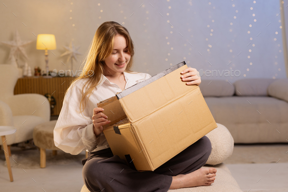 Excited young woman unpacking huge carton box, looking inside Stock Photo by  kolesnikovsergii