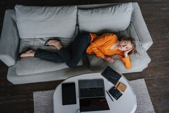 Overworked businesswoman in orange blouse and black pants laying on couch, feels fatigue.