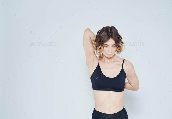 A strange woman in a short T-shirt has joined her hands behind her back on a light background