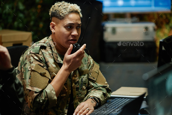 Young multiethnic female officer of surveillance center using walkie-talkie