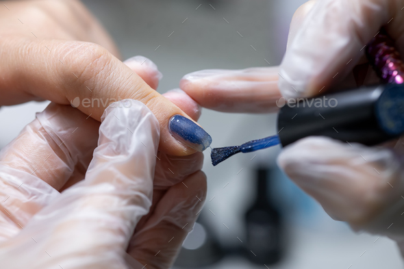 the nail service master makes a manicure by distributing blue gel polish with a nail brush