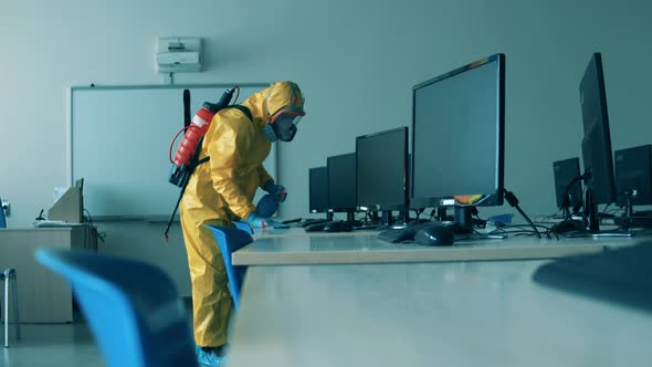 Covid19, Coronavirus Concept. Worker in Hazmat Sanitizes Desks with Computers. alt