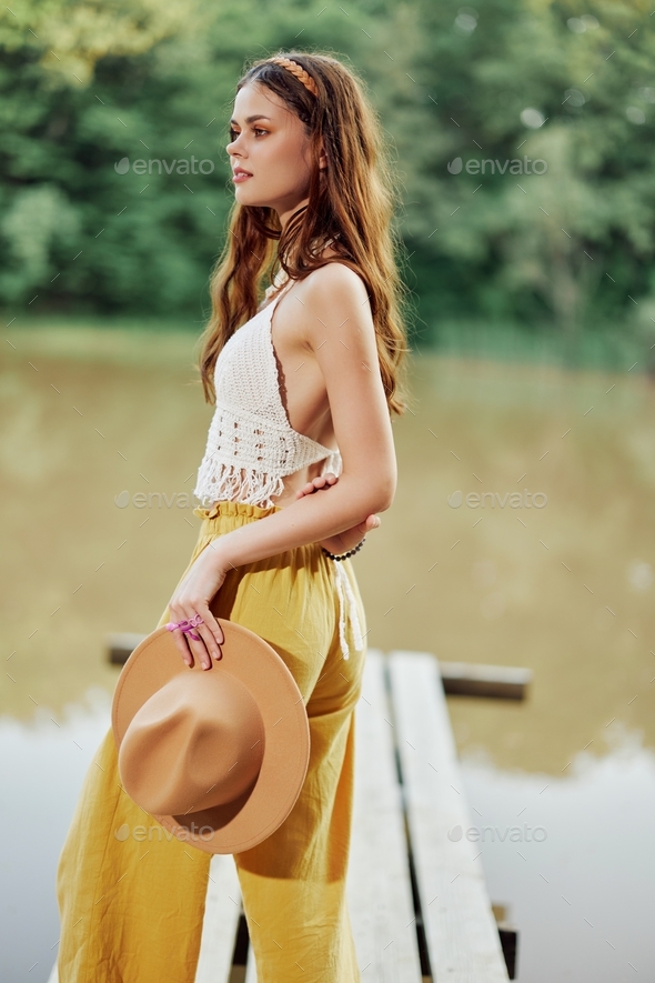 A young woman smiling in an image of a hippie and eco-dress dancing in nature by the lake wearing a