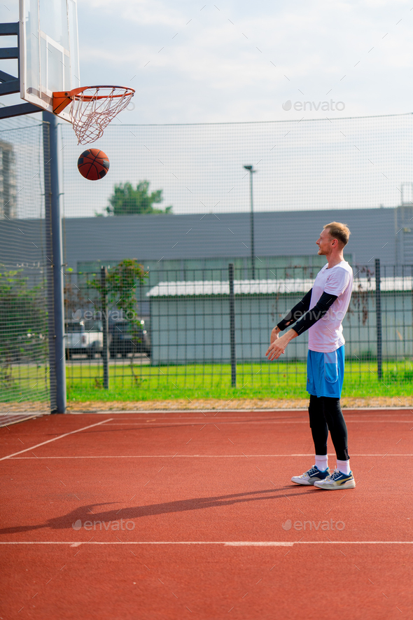 tall guy basketball player throws a ball into a basketball hoop at a