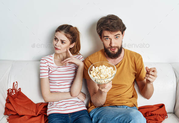 A man and a woman on the couch watching TV with popcorn in a plate
