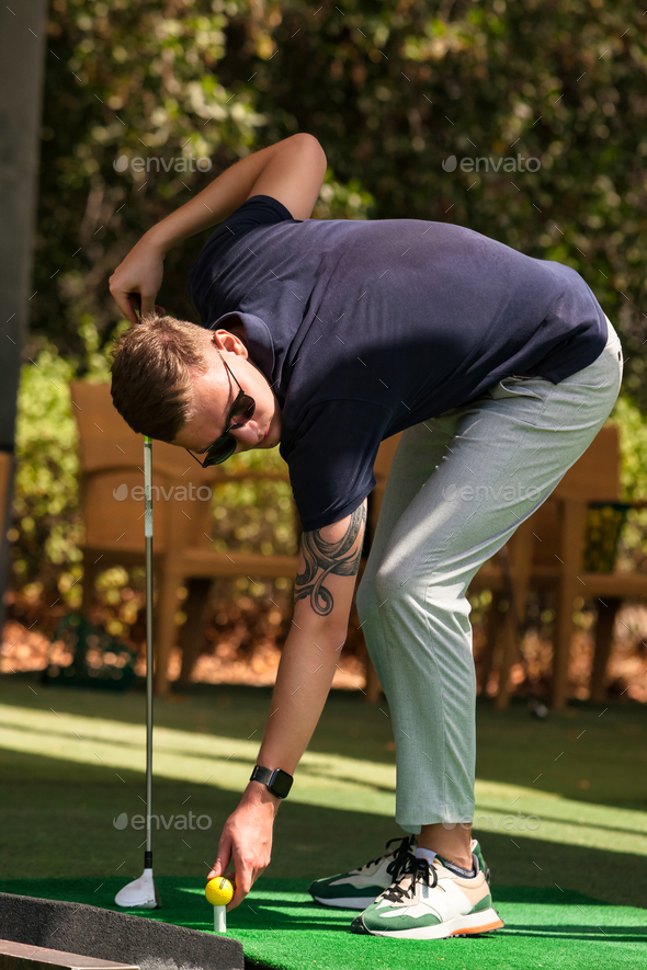 Confident golfer young guy in sunglasses with golf club taking ball posing in golf course