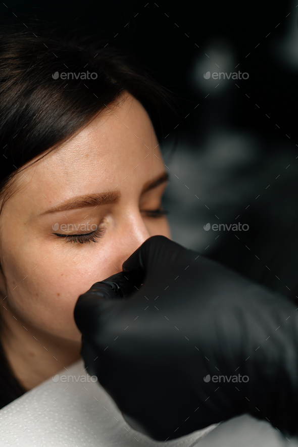 Piercing process Professional nose piercing for a girl the master pierces the nose with needle