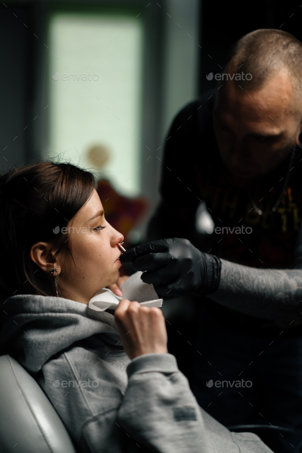 Piercing process Professional nose piercing for a girl the master pierces the nose with needle