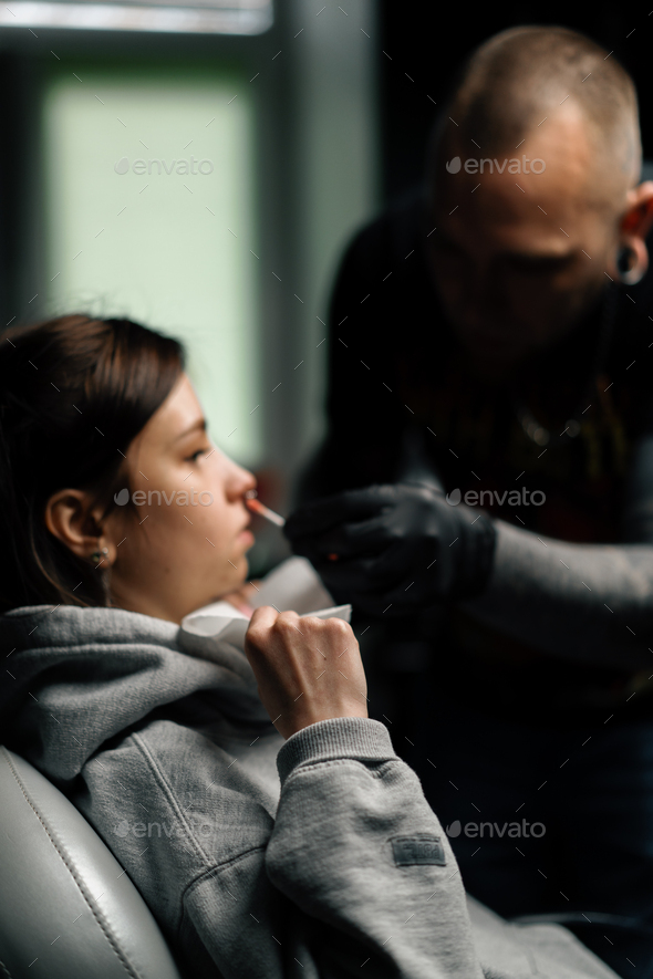 Piercing process Professional nose piercing for a girl the master pierces the nose with needle