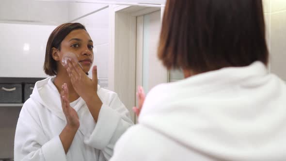 A Young Beautiful Woman Looks in the Mirror and Uses Foam to Clean Her Face