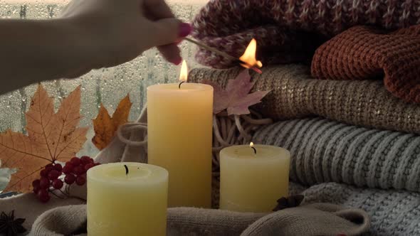 Hand with Burning Match Lighting Candle on Cozy Knitted Sweater in Warm Yellow Lights alt
