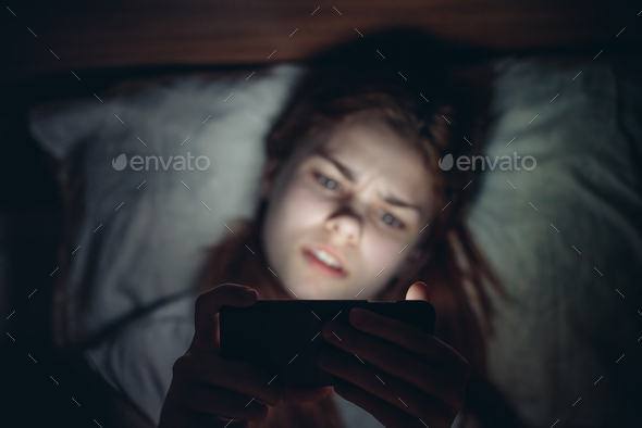 woman lying in bed with phone in hand watching news before bedtime
