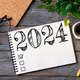 2024 New year resolutions on desk. 2024 goals list with notebook, coffee cup, plant on wooden table - PhotoDune Item for Sale