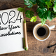 2024 New year resolutions on desk. 2024 goals list with notebook, coffee cup, plant on wooden table - PhotoDune Item for Sale