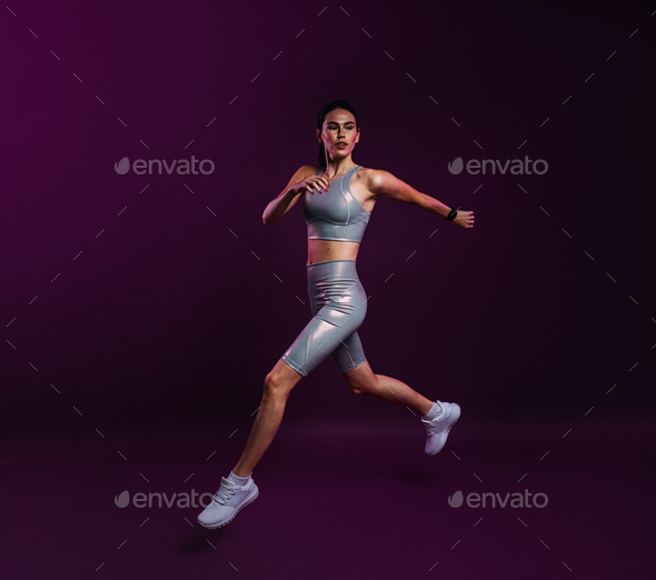 Young slim female in silver fitness attire running against a magenta  background Stock Photo by ArtemVarnitsin
