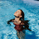 Happy woman swimming in pool in red swimsuit with loose long hair